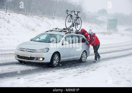 Mitglied des Nordens Dartmoor Such- und Rettungsteam helfen puxh ein Auto fahren entlang einer Straße in der Nähe von Okehampton in Devon als schweren Schnee Verkehrschaos zu Teilen der South West gebracht. Stockfoto