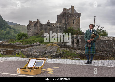 Dornie, Schottland - 10. Juni 2012: Einzelspieler in schottischer Tracht vor dem Eilean Donan Castle aus braunem Stein. Bei starkem Regen Stockfoto