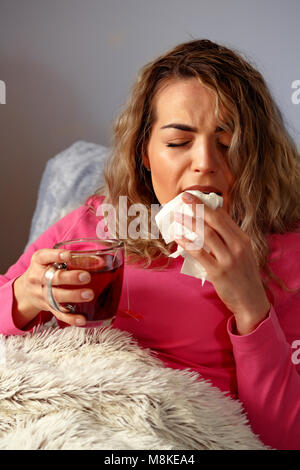 Junge Frau krank im Bett mit Temperatur trinken heißen Tee zu Hause. Stockfoto