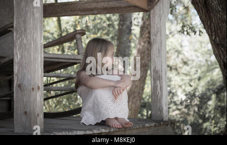 Kleines Mädchen sitzt auf einer Veranda barfuß Stockfoto