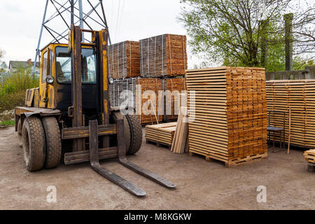 Große Gabelstapler und Stapel von neuen Holzbrettern und Nieten an den Holzplatz. Holzplatten auf Pfählen für Möbel-Materialien Stockfoto