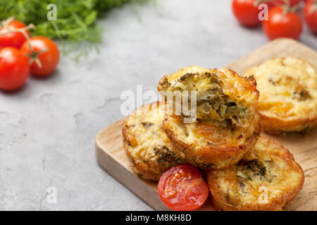 Gesundes Frühstück. Brokkoli Käse beißt (Muffins), frische Tomaten, frischen Kräutern auf grauem Beton Hintergrund Stockfoto