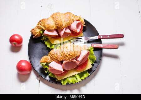 Licht und herzhaften Frühling Frühstück. Croissant mit Schinken, Käse, frische Tomaten auf einem weißen Tisch aus Stein. Stockfoto