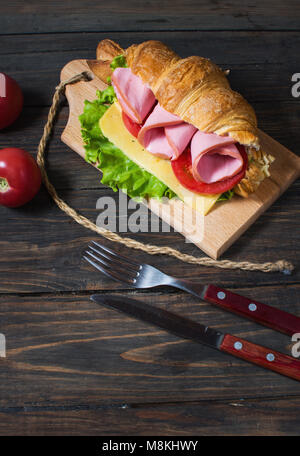 Licht und herzhaften Frühling Frühstück. Croissant mit Schinken, Käse, frische Tomaten auf einem Holz Tisch aus Stein. Stockfoto