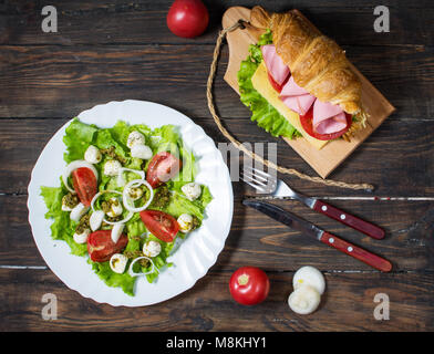 Licht und herzhaften Frühling Frühstück. Croissant mit Schinken, Käse, frischen Tomaten und Salat mit Mozzarella auf einem Holz Tisch Stockfoto