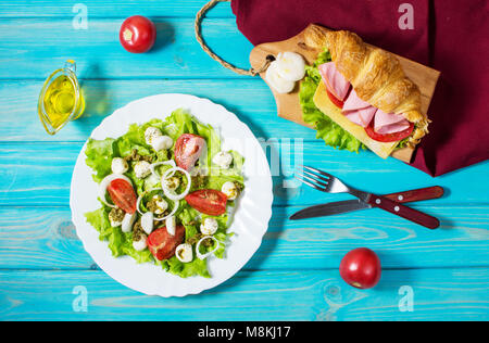 Licht und herzhaften Frühling Frühstück. Croissant mit Schinken, Käse, frischen Tomaten und Salat mit Mozzarella auf einem Holz Tisch Stockfoto