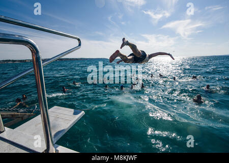 Junger Mann Tauchen in Meer und die Gruppe der Freunde im Meer schwimmen auf einem Boot Ausflug Stockfoto