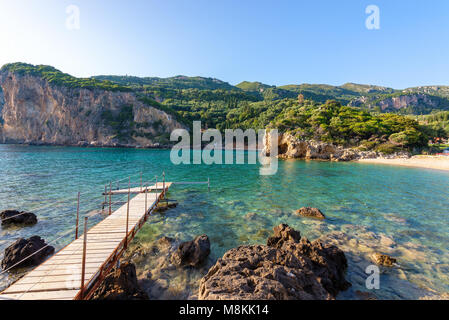 Hölzerne Seebrücke in Paleokastritsa Bucht mit Sand und kristallklares Meerwasser. Insel Korfu, Griechenland. Stockfoto