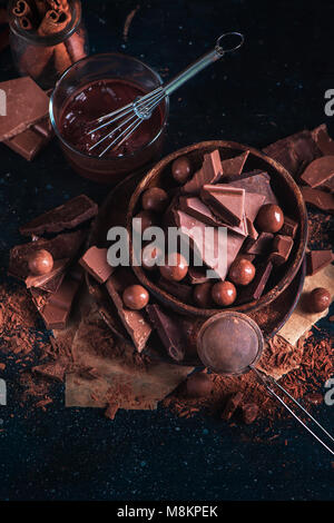 Hölzerne Schüssel mit hausgemachten Pralinen und Schokolade Stücke, Verglasung mit einem Schneebesen, verstreute Kakaopulver auf einem dunklen Hintergrund. Dessert Zutaten Clos Stockfoto