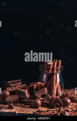 Dessert Zutaten close-up. Zimt in einem Glas, verstreute Kakaopulver und zerbrochenes Schokolade auf einem dunklen Hintergrund mit kopieren. Stockfoto