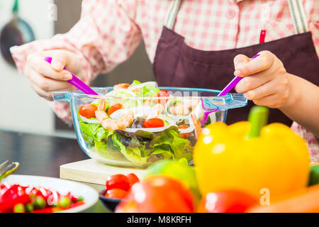 Frau Koch frische Garnelen Salat in Ihrem Haus kochen, verschiedene Gemüse auf den Tisch und zeigt ihre Hand Holding utencils Mischen der Salat, bis w Schließen Stockfoto