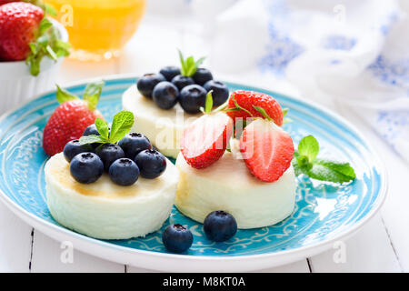 Mini Käsekuchen mit frischen Erdbeeren und Heidelbeeren auf blauen Platte, Detailansicht. Syrniki, Quark Pfannkuchen Stockfoto