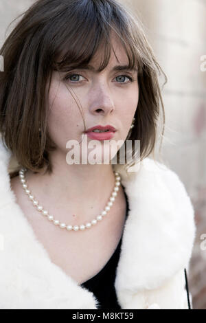 Eine Frau mit roten Lippenstift, trägt einen weissen Fell Jacke und eine Perlenkette. Stockfoto