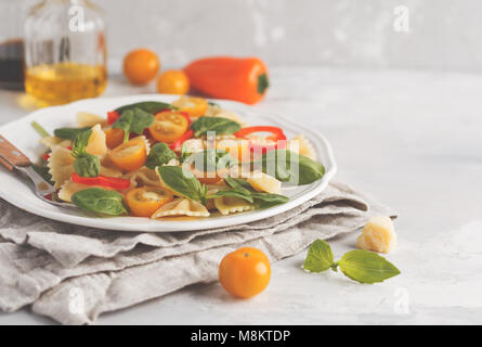 Italienische Pasta farfalle Salat mit Gemüse, Basilikum und Spinat in eine weiße Platte. Hellen Hintergrund Stockfoto