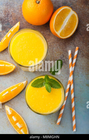 Zwei Gläser mit frisch gepresstem Orangensaft und Minze auf einem alten rostigen blauen Hintergrund. Ansicht von oben Stockfoto