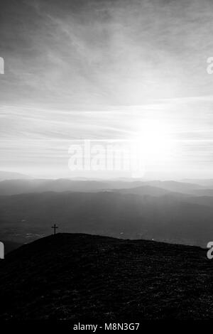 Kreuz auf dem Gipfel des Mt. Serrasanta (Umbrien, Italien), mit Sun niedrig am Horizont Stockfoto