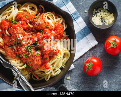 Spaghetti mit Fleischbällchen in Tomatensoße und Parmesan in eine eiserne Pfanne über strukturierten Hintergrund. Ansicht von oben. Stockfoto