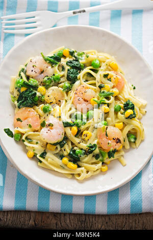 Cremige King Prawn Tagliatelle mit Erbsen, Spinat und Mais Stockfoto