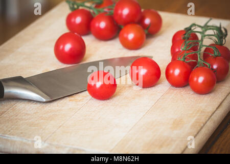 Cherry Tomaten (Solanum Lycopersicum) und ein Messer auf einem hölzernen Schneidebrett Stockfoto