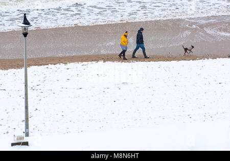 Paar mit Hund entlang der Küste mit Bournemouth Strand Meer in Schnee am Bournemouth, Dorset, England UK im März abgedeckt Stockfoto