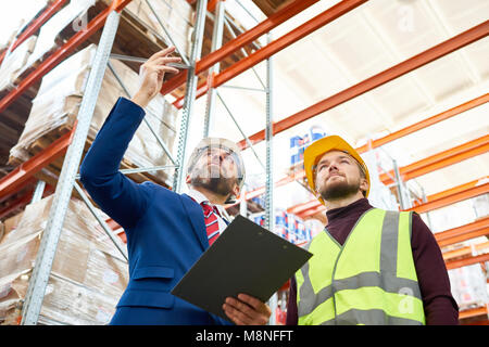 Low Angle Portrait von Warehouse Manager holding Zwischenablage sprechen für die Beschäftigten tragen, hardhat und reflektierende Jacke beim Besprechen von Lagerbestand Stockfoto