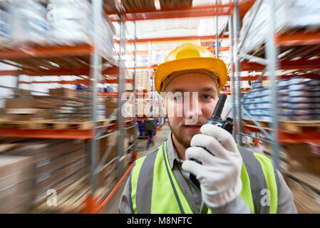 Porträt der jungen Lagerarbeiter spricht von walkie-talkie stehend gegen hohen Regalen im Lagerhaus, kopieren Raum Stockfoto