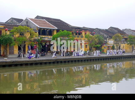 Hoi An, Vietnam - MÄRZ 17, 2018: die große Gruppe der jungen Mädchen in der Vietnamesischen traditionellen Kleid in Hoi An Altstadt mit Blick auf die typische gelbe Häuser Stockfoto