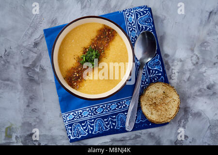Lila porzellan Schale, cremige Kürbissuppe mit Dill garniert, serviert mit getoasteten Brotscheiben auf homespun Serviette über weiße strukturierte Hintergrund, Stockfoto