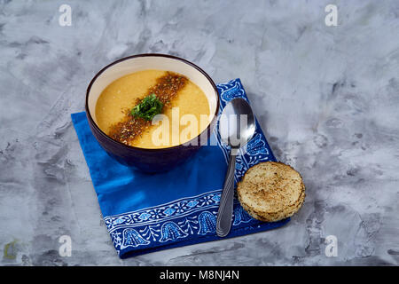 Lila porzellan Schale, cremige Kürbissuppe mit Dill garniert, serviert mit getoasteten Brotscheiben auf homespun Serviette über weiße strukturierte Hintergrund, Stockfoto