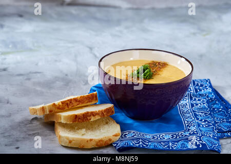 Lila porzellan Schale, cremige Kürbissuppe mit Dill garniert, serviert mit getoasteten Brotscheiben auf homespun Serviette über weiße strukturierte Hintergrund, Stockfoto