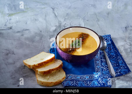 Lila porzellan Schale, cremige Kürbissuppe mit Dill garniert, serviert mit getoasteten Brotscheiben auf homespun Serviette über weiße strukturierte Hintergrund, Stockfoto