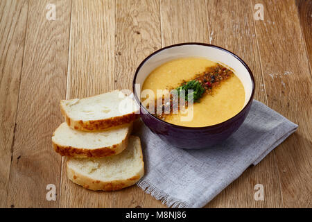 Lila Schale, cremige Kürbissuppe mit Dill garniert, serviert mit getoasteten Brotscheiben mit Paste auf homespun Serviette über rustikale Hintergrund, Stockfoto