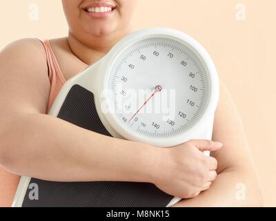 Übergewichtige Frau mit Waage, lächelnd. Stockfoto