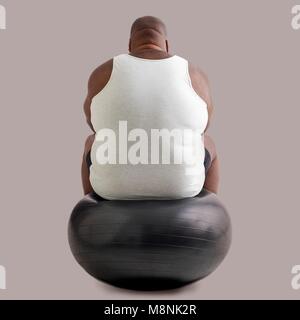 Übergewicht Mann sitzt auf einer übung Kugel, Ansicht von hinten. Stockfoto