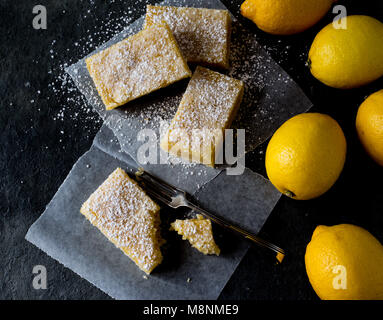 Lemon Bars und Zitronen auf Wachspapier dunklen Hintergrund overhead Shot Stockfoto