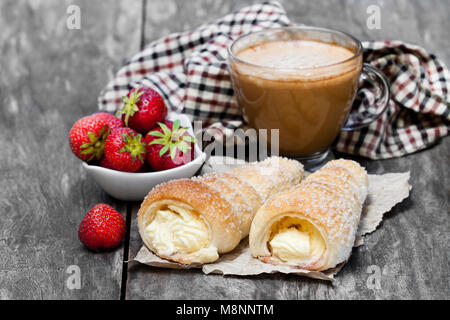 Blätterteig Hörner mit Tasse Cappuccino und Erdbeere auf hölzernen Tisch Stockfoto