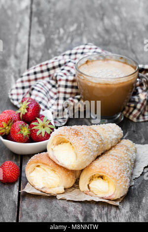 Blätterteig Hörner mit Tasse Cappuccino und Erdbeere auf hölzernen Tisch Stockfoto