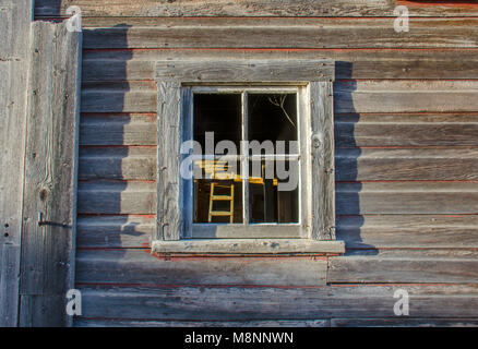Die Wand eines alten Bauernhaus mit einem Fenster, die Treppe im Inneren der Scheune leuchtet durch Sonnenlicht Stockfoto