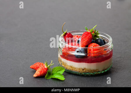 Mini wilden Wald Beeren Käsekuchen in einem Glas Topf auf schwarzen Stein Hintergrund Stockfoto