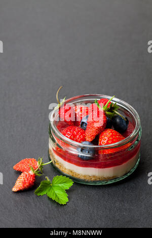 Mini wilden Wald Beeren Käsekuchen in einem Glas Topf auf schwarzen Stein Hintergrund Stockfoto