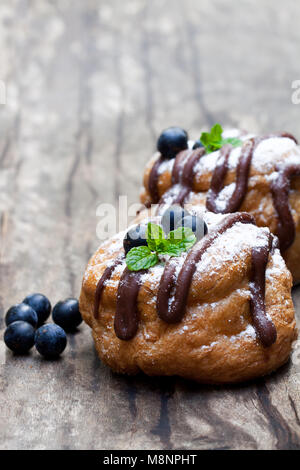 Die belgische Schokolade choux Brötchen gefüllt mit Heidelbeeren und Creme auf hölzernen Tisch Stockfoto