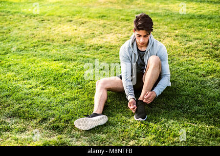 Läufer in der Stadt sitzen auf Gras Schnürsenkel binden. Stockfoto