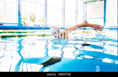 Älterer Mann Schwimmen im Innenpool. Stockfoto