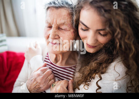 Ein junges Mädchen mit Großmutter zu Hause, umarmen sich. Stockfoto