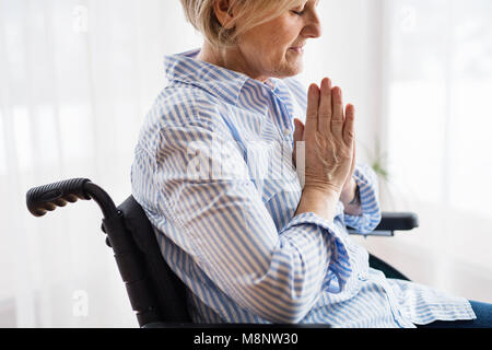 Eine ältere Frau im Rollstuhl zu Hause beten. Stockfoto