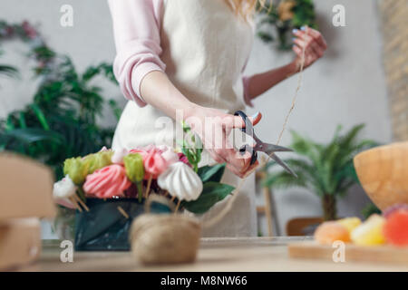 Foto von Floristen mit Scheren - Schneiden von Seilen am Tisch mit Blumenstrauß, Marmelade, Eibisch im Zimmer Stockfoto