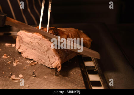 Gebratenes Fleisch von Truthühnern mit Fleischmesser und Gabel und Küchenchef im Hintergrund geschnitzt Stockfoto