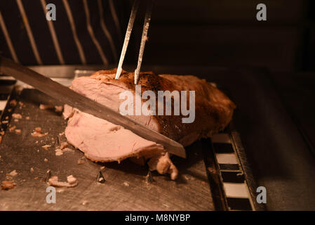 Gebratenes Fleisch von Truthühnern mit Fleischmesser und Gabel und Küchenchef im Hintergrund geschnitzt Stockfoto