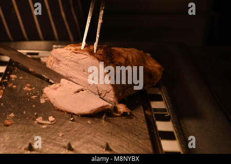 Gebratenes Fleisch von Truthühnern mit Fleischmesser und Gabel und Küchenchef im Hintergrund geschnitzt Stockfoto