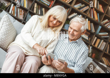 Im Alter von Mann und Frau zusammen zu Hause im Wohnzimmer sitzen Sie ihr Smartphone berühren Bildschirm lächeln Stockfoto